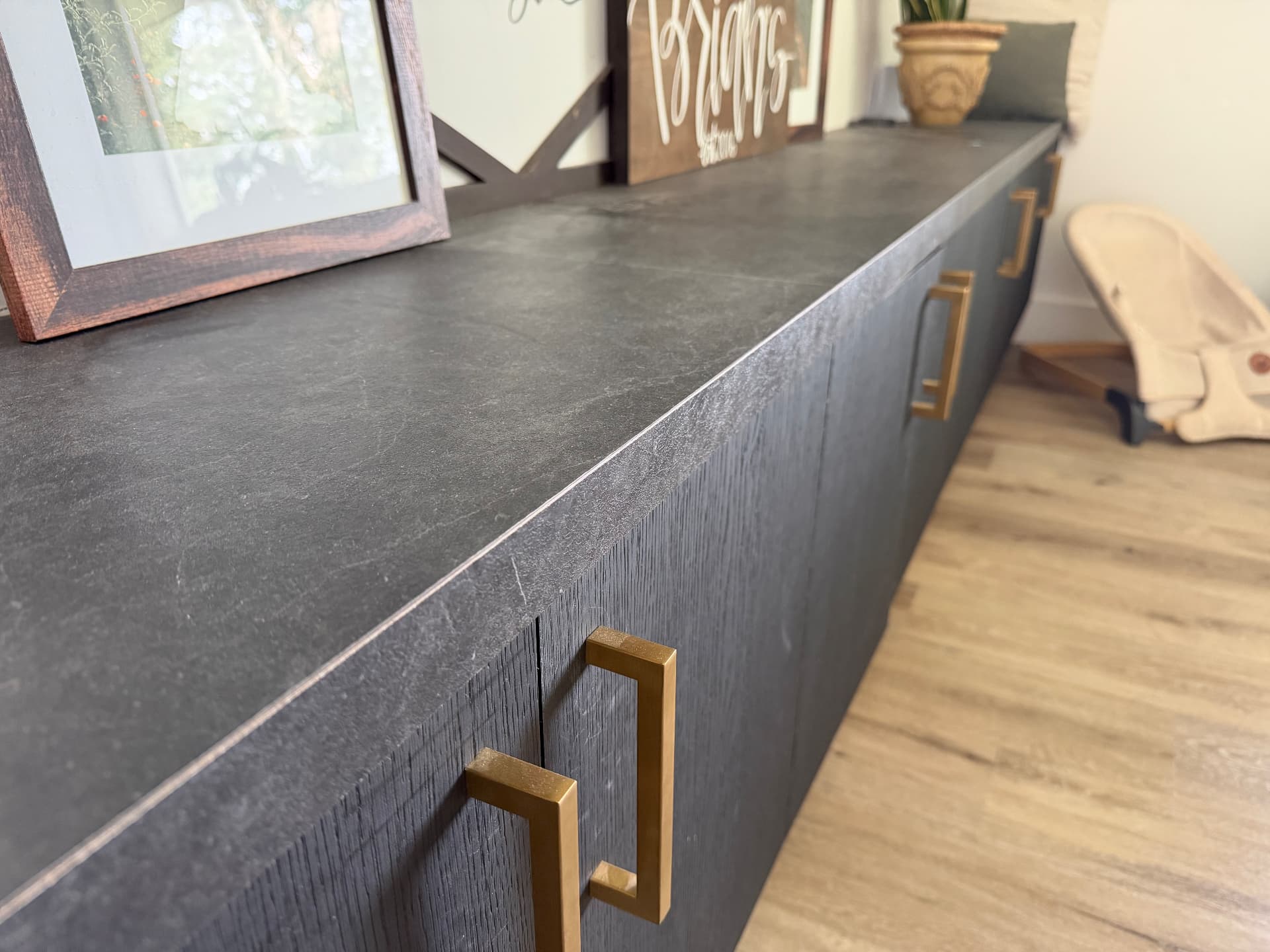 Long dark slate-look laminate top with a crisp square edge over black oak cabinets with brass pulls